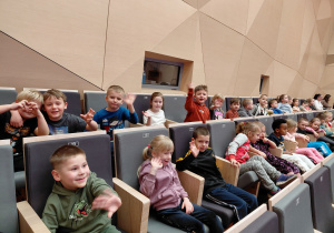 Dzieci siedzą w fotelch na sali koncertowej Szkoły Muzycznej.