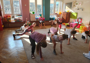 Dzieci w wykroku z uniesiona ku górze jedną ręką.