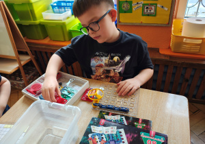 Chłopiec siedzi przy stole i układa na plastikowej planszy elementy "Sekretów elektroniki".