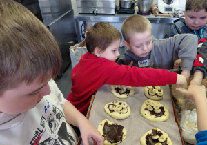 Chłopcy dekorują uformowane bułki bananami.