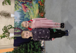 Chłopiec i dziewczynka stoją na dywanie. W tle obrazek lasu i chatki.