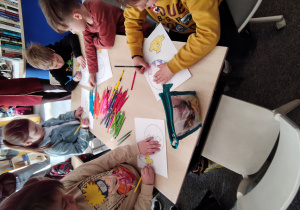 Czterech chłopców i jedna dziewczynka siedzą przy stole i kolorują kurczaczka i pisankę.