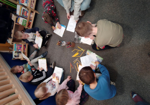 Przedszkolaki siedzą i leżą kolorując kurczaczka i pisankę.