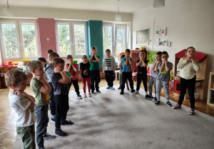 Przedszkolaki stoją w półkolu i trzymają pięści pod brodą.