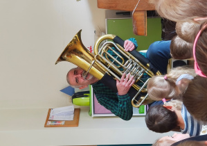 Mężczyzna w koszuli w kratę gra na tubie siedząc na krześle.