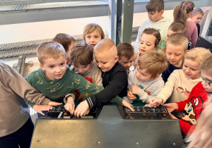 Przedszkolaki stoją przy maszynie do kierowania tramwajem.