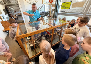 Przedszkolaki wraz z przewodnikiem stoją przy gablotce z eksponatem "silnika" tramwaju.