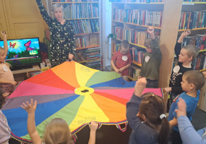 Przedszklaki wraz z panią bibliotekarką bawią się chustą animacyjną.