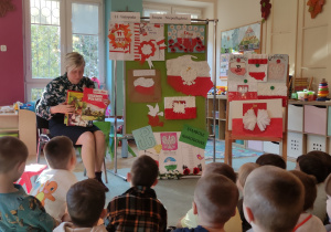 Pani Bibliotekarka pokazuje książkę o Polsce siedzącym dzieciom, w tle prace plastyczne o Polsce.