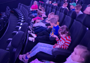 Przedszkolaki siedzą w fotelach sali kinowej Planetarium.