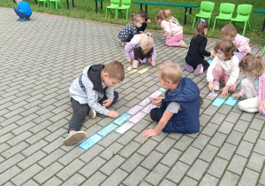 Przedszkolaki rysują kredą na kostce tarasu przedszkolnego.