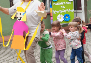 Nauczycielka wraz z dziećmi idzie w wężyku na tarasie przedszkolnym.