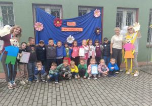 Przedszkolaki wraz z nauczycielkami i Panią Dyrektor pozują do zdjęcia na tle dekoracji Dnia Przedszkolaka.