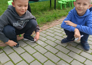 Chłopcy rysują kredą na kostce tarasu przedszkolnego.