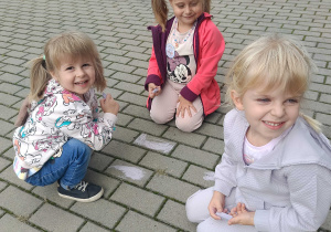 Przedszkolaki rysują kredą na kostce tarasu przedszkolnego.