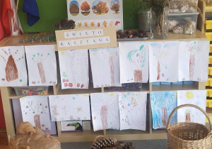 Wystawa prac plastycznych wykonanych przez dzieci - drzewa. Przed wystawą stoi figurka jeża, koszyk z szyszkami i kosz wiklinowy.