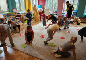 Przedszkolaki biegają po dywanie. Dotykają zielonych i czerwonych krążków leżących na dywanie.