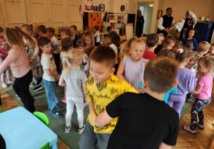 Przedszkolaki tańczą w parach. Mężczyzna z kobietą w strojach regionalnych również tańczą. w kole.