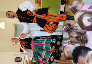Mężczyzna z kobietą w strojach regionalnych podskakują trzymając się za ręce.