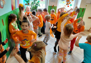 Przedszkolaki ubrane na pomarańczowo tańczą.