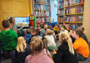 Przedszkolaki siedzą na dywanie. Pani z biblioteki czyta dzieciom książkę o jesieni.