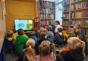 Przedszkolaki siedzą na dywanie i oglądają program edukacyjny o jesieni.