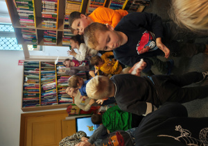 Przedszkolaki stoją w rozsypce na dywanie. Dmuchają w białe piórka.