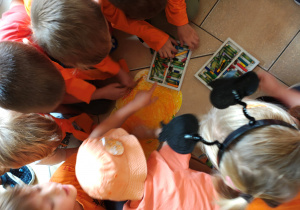 Przedszkolaki siedzą na podłodze i malują pastelami papierową dynię.