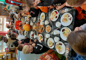 Przedszkolaki przebrane na Halloween siedzą przy stole z halloweenowymi dekoracjami i jedzą drugie śniadanie.