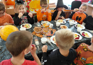 Przedszkolaki przebrane na Halloween siedzą przy stole z halloweenowymi dekoracjami i jedzą drugie śniadanie.