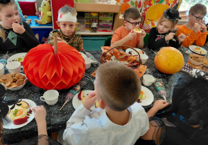 Przedszkolaki przebrane na Halloween siedzą przy stole z halloweenowymi dekoracjami i jedzą drugie śniadanie.