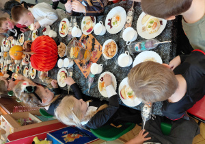 Przedszkolaki przebrane na Halloween siedzą przy stole z halloweenowymi dekoracjami i jedzą drugie śniadanie.