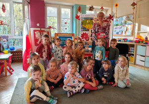 Przedszkolaki z grupy I wraz z Panią bibliotekarką stoją na dywanie, za nimi stoją dekoracje z okazji Święta Niepodległości oraz prace na konkurs "Symbole narodowe".