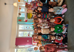 Przedszkolaki z grupy III wraz z Panią bibliotekarką stoją, część dzieci siedzi na dywanie, za nimi stoją dekoracje z okazji Święta Niepodległości oraz prace na konkurs "Symbole narodowe".