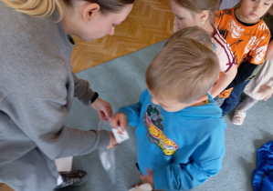 Chlopiec wybiera naklejkę z torby, którą trzyma pani od warsztatów.