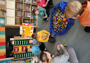 Przedszkolaki siedzą na dywanie. Na środku leży duża torba z klockami LEGO.