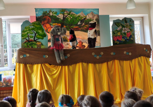 Przedszkolaki siedzą tyłem na dywanie. Przed nimi scenografia i kukły słonia, bobra i sroki.