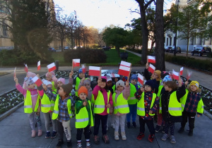 Przedszkolaki ubrane w odblaskowe kamizelki z flagami Polski przed Grobem Nieznanego Żołnierza.