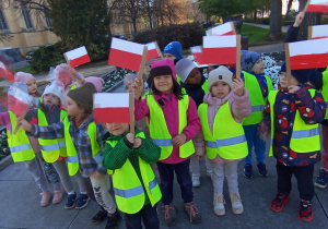 Przedszkolaki ubrane w odblaskowe kamizelki z flagami Polski przed Grobem Nieznanego Żołnierza.