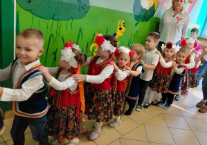 Przedszkolaki ubrane na galowo, w regionalnych kamizelkach stoją tworząc wężą.