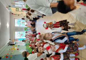 Przedszkolaki wraz z paniami, ubrane na galowo i w regionalnych kamizelkach idą w parach i trójkach po kole.