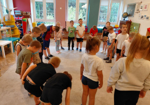 Przedszkolaki w strojach sportowych stoją w kole z pochylonymi głowami.