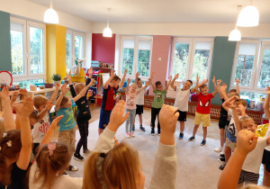 Przedszkolaki w strojach sportowych stoją w kole z rękoma w górze.