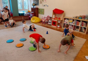 Chłopiec przechodzi po sensorycznych kołach, trzech chlopców przechodzi jak raczki między pachołkami.