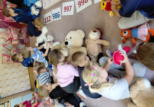 Przedszkolaki siedzą na dywanie, nachylają się nad pluszakami.