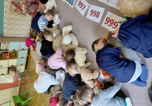 Przedszkolaki siedzą na dywanie, nachylają się nad pluszakami.