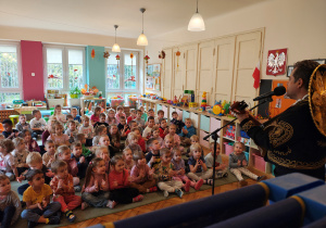 Przedszkolaki siedzą na dywanie. Mężczyzna z gitarą i sombrero stoi przed dziećmi.