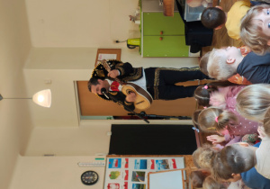 Przedszkolaki siedzą tyłem na dywanie. Mężczyzna z gitarą i sombrero stoi przed dziećmi.