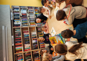 Przedszkolaki siedzą przy stole i na fotelach.