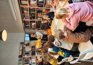 Przedszkolaki siedzą przy stole. Bibliotekarka pokazuje im książkę.
